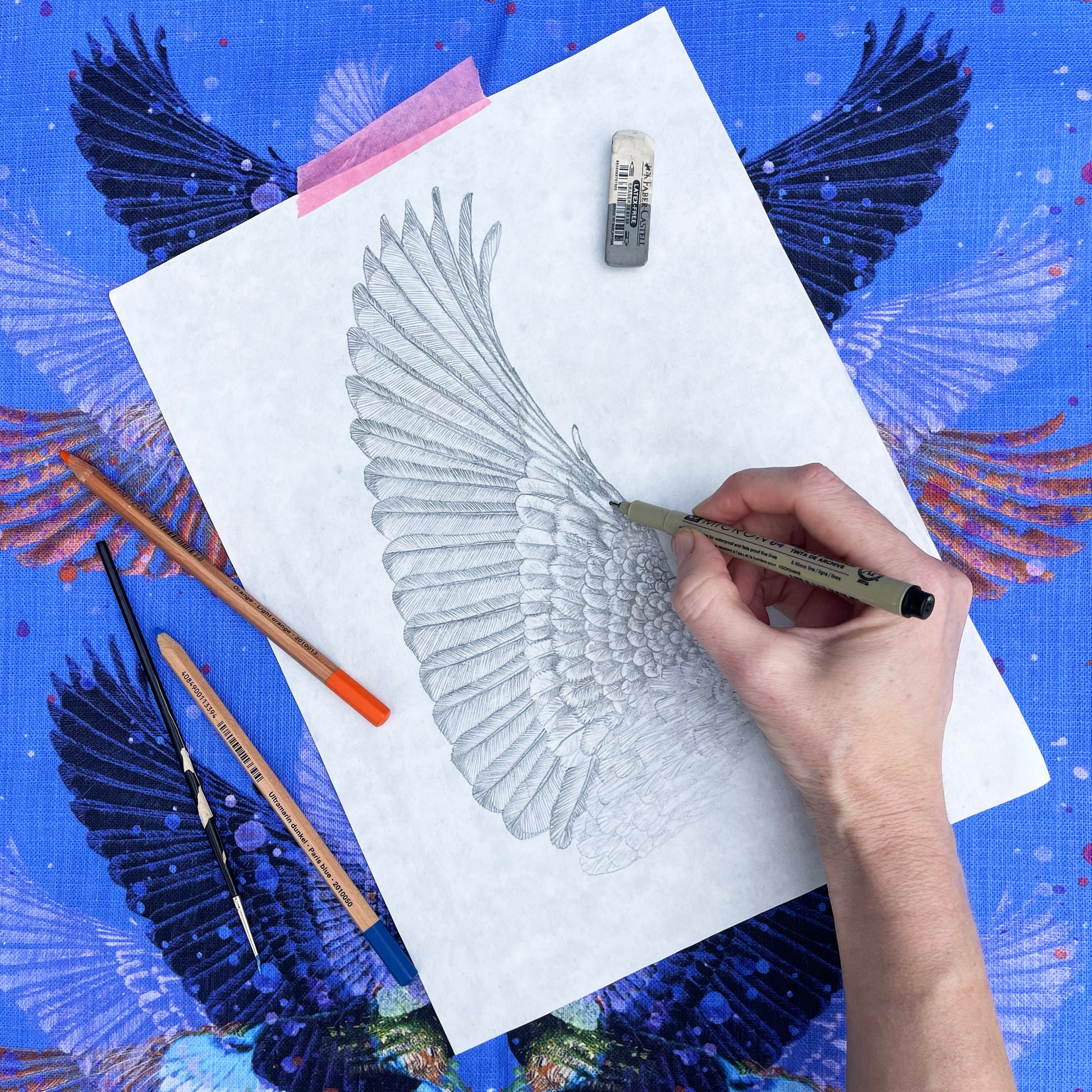 Hand drawing a detailed wing on paper with art supplies around